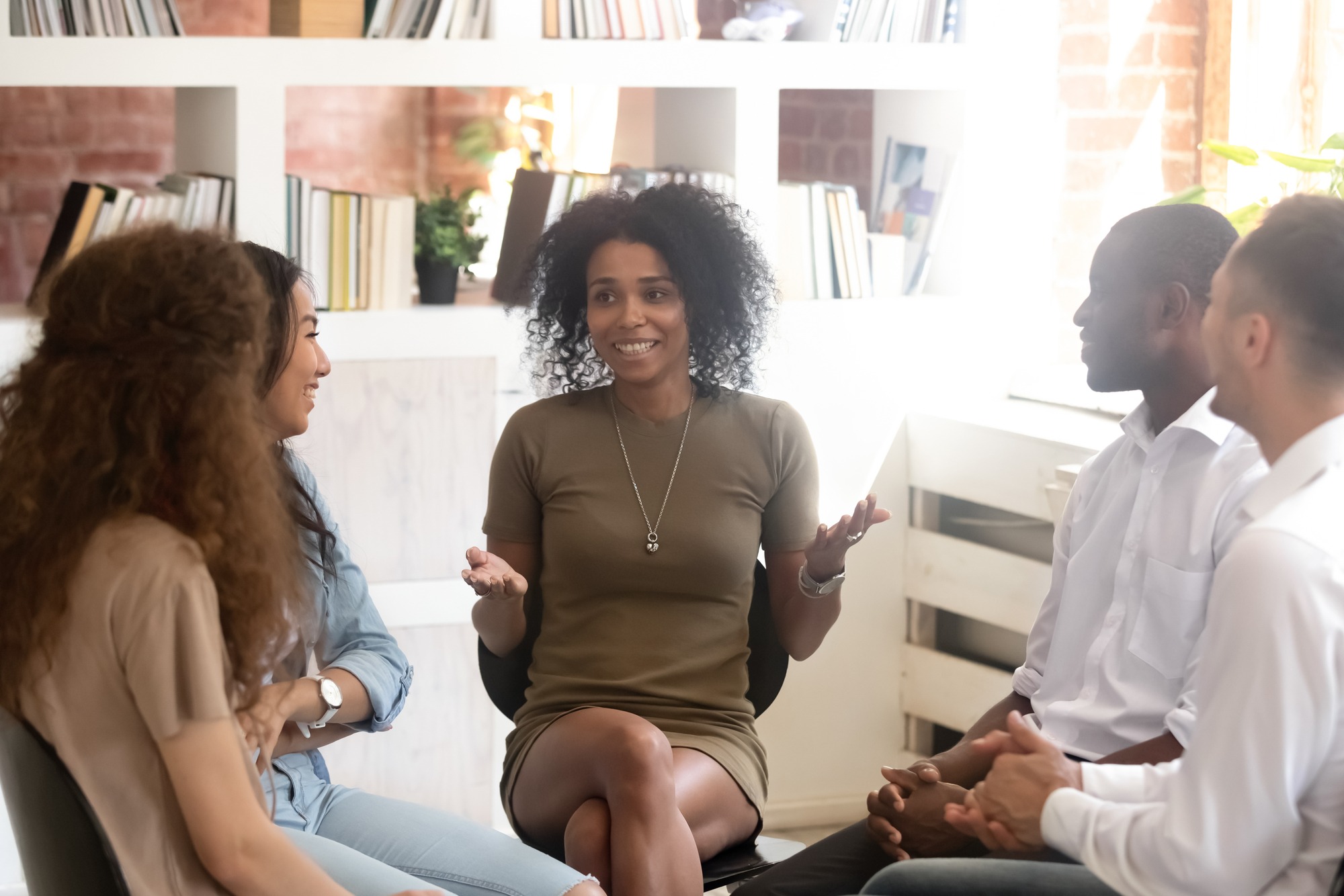 A woman with curly hair engaged in conversation with three people in a modern, brightly lit room, promoting collaboration and discussion.