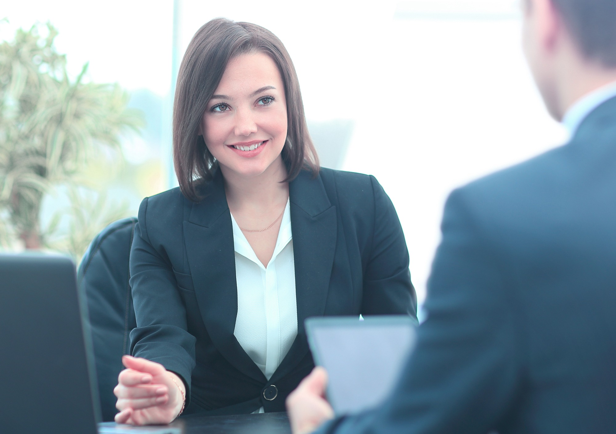 A professional woman in a suit smiles and extends her hand during a meeting, highlighting a positive and engaging business interaction.